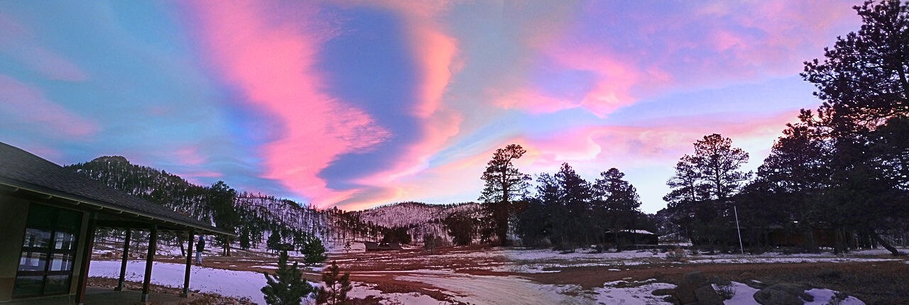 A beautiful vibrant pink and blue sunset showing clouds wavering over the ponderosa pine-filled valley of Drala Mountain Center